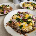 Three bowls filled with shredded beef, a fried egg and garnishes of purple onion, cilantro and cheese to make Chilaquiles & Eggs.
