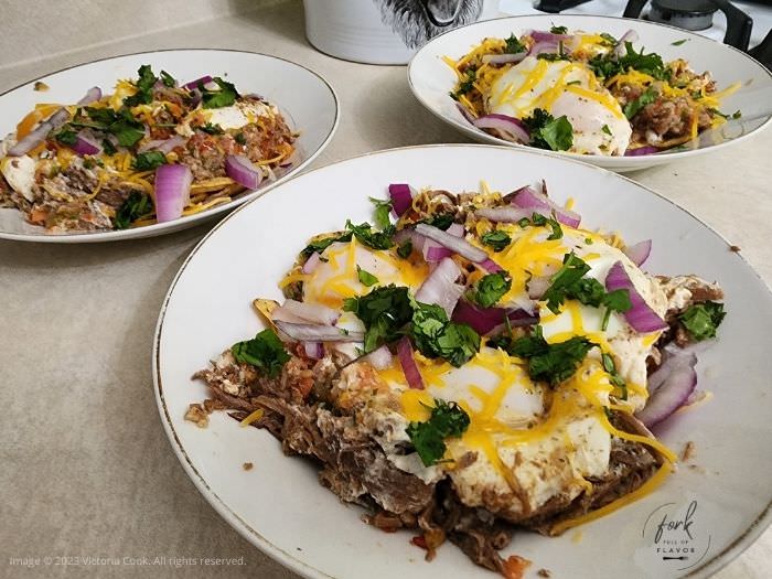 Three bowls filled with shredded beef, a fried egg and garnishes of purple onion, cilantro and cheese to make Chilaquiles & Eggs.