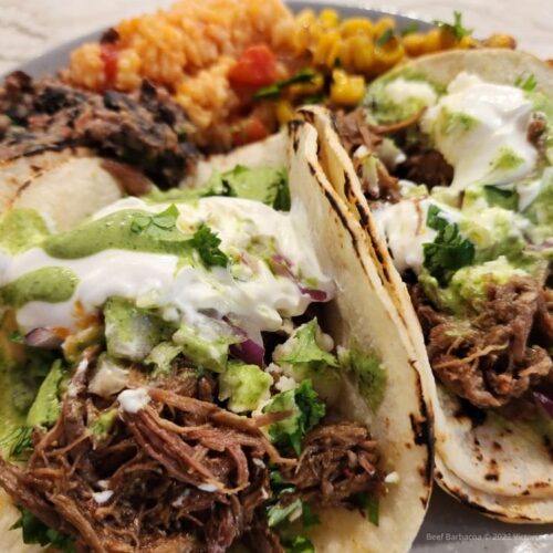 Beef Barbacoa tacos on a plate with Mexicans rice and beans in the background.