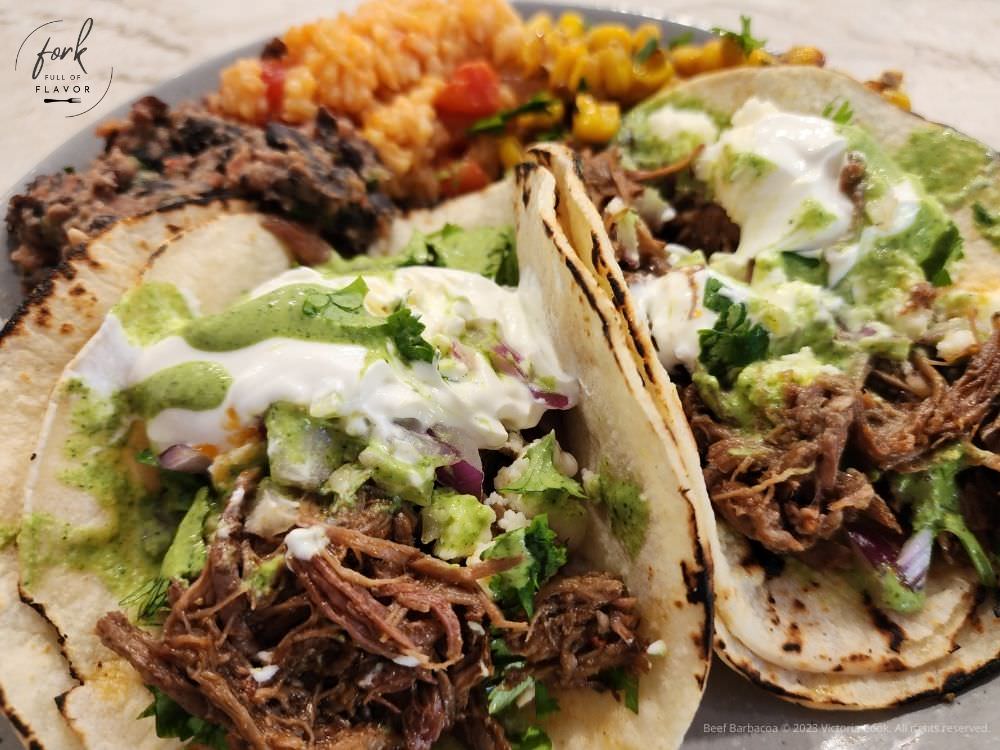 Beef Barbacoa tacos on a plate with Mexicans rice and beans in the background.