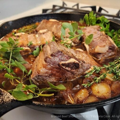 A cast iron skillet of braised beef short ribs and herbs