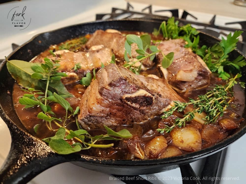 A cast iron skillet of braised beef short ribs and herbs