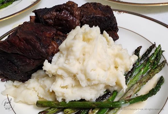 Plated braised beef short ribs with mashed potatoes, and asparagus in a beurre blanc sauce