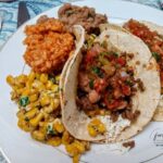 A taco meal with Mexican Rice, beans and Mexican Street Corn.