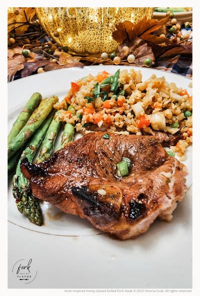 Asian-Inspired Honey Glazed Grilled Pork Steak plated with asparagus and cauliflower fried rice.