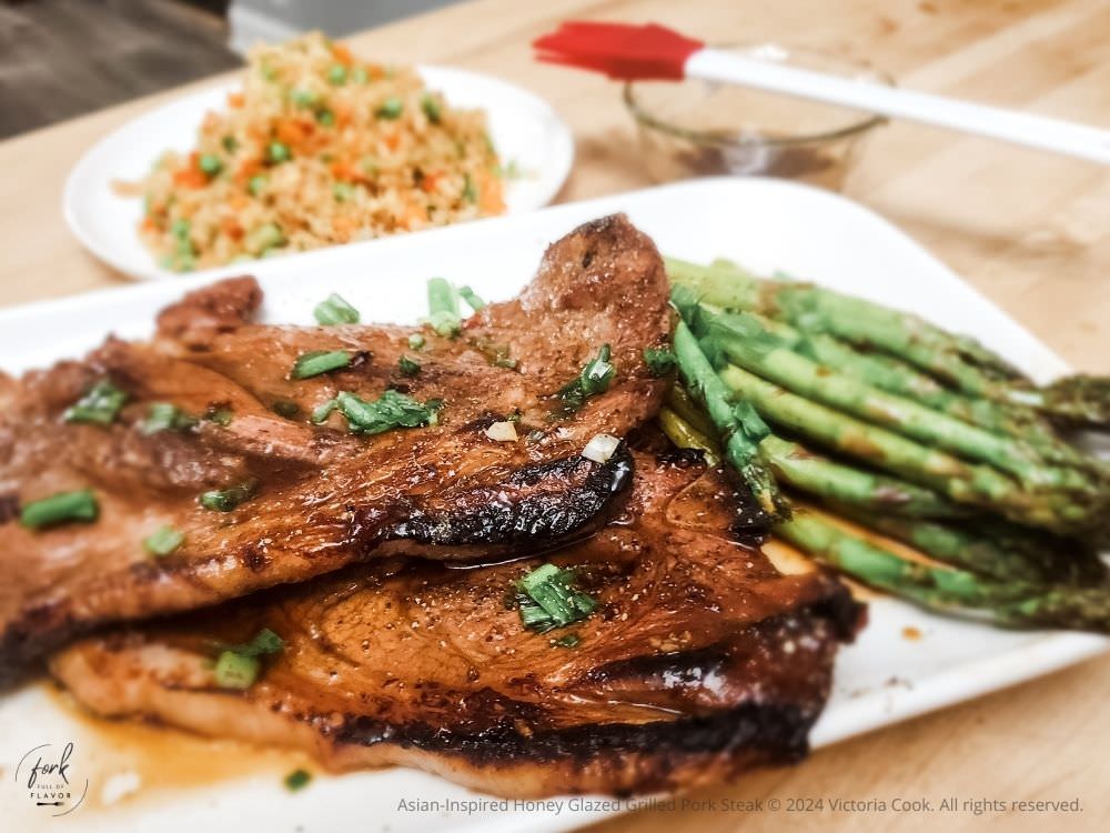 Asian-Inspired Honey Glazed Grilled Pork Steak plated with grilled asparagus and cauliflower fried rice