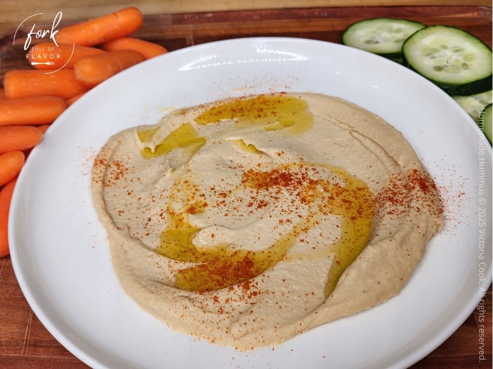 Homemade Hummus - Hero Homemade hummus plated and topped with a drizzle of olive oi l and a couple shakes of paprika ready to eat with some baby carrots and sliced cucumbers.