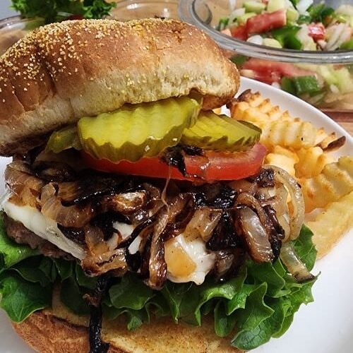 A gourmet beef burger loaded with lettuce, tomato, cheese, grilled onions and pickles on a toasted bun.