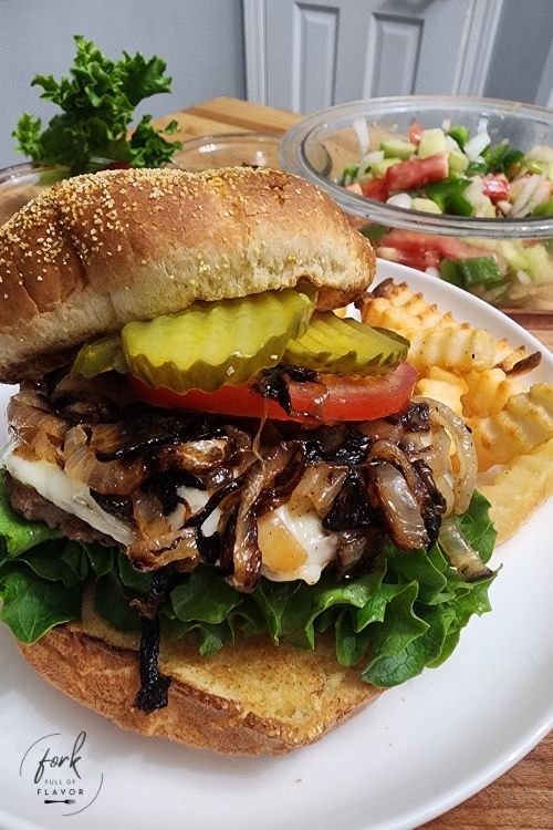 Gourmet Burgers single photo vertical A gourmet beef burger loaded with lettuce, tomato, cheese, grilled onions and pickles on a toasted bun.