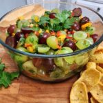 A bright bowl of green and purple grapes made into grape salsa garnished with cilantro and served with corn chips.