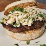 Sesame Pork Burger on a toasted English Muffin and topped with spicy slaw and garnished with chopped cilantro.