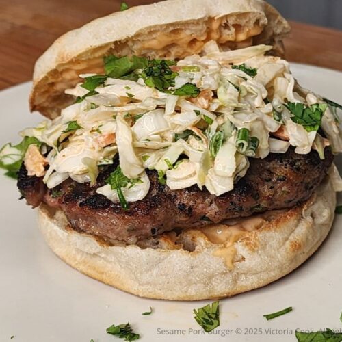 Sesame Pork Burger on a toasted English Muffin and topped with spicy slaw and garnished with chopped cilantro.