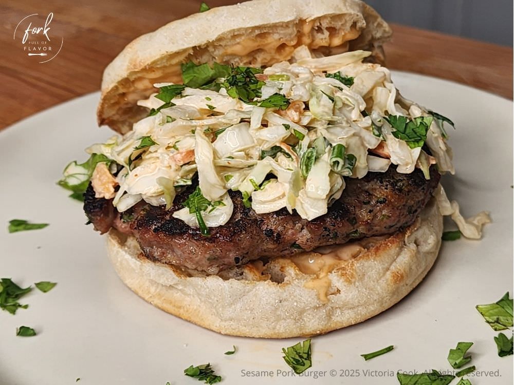 Sesame Pork Burger on a toasted English Muffin and topped with spicy slaw and garnished with chopped cilantro.
