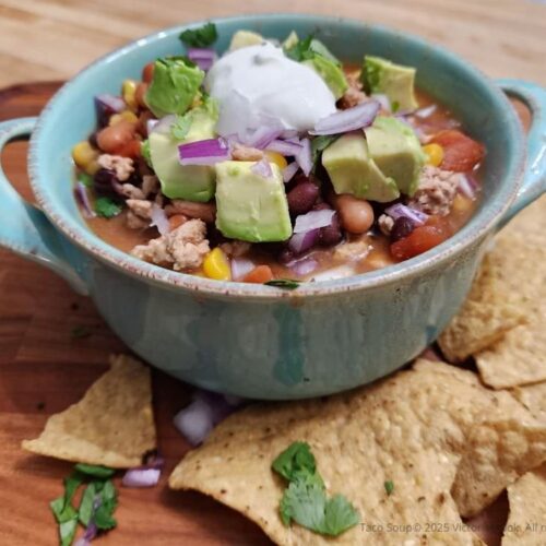 A hearty bowl of taco soup with pinto and black beans, and topped with avocado, cilantro, and sour cream.