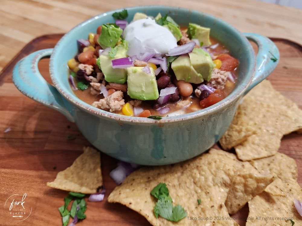 Taco Soup - Hero Image A hearty bowl of taco soup with pinto and black beans, and topped with avocado, cilantro, and sour cream.