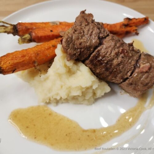 Beef Rouladen atop mashed potatoes and accompanied by roasted carrots on a plate.