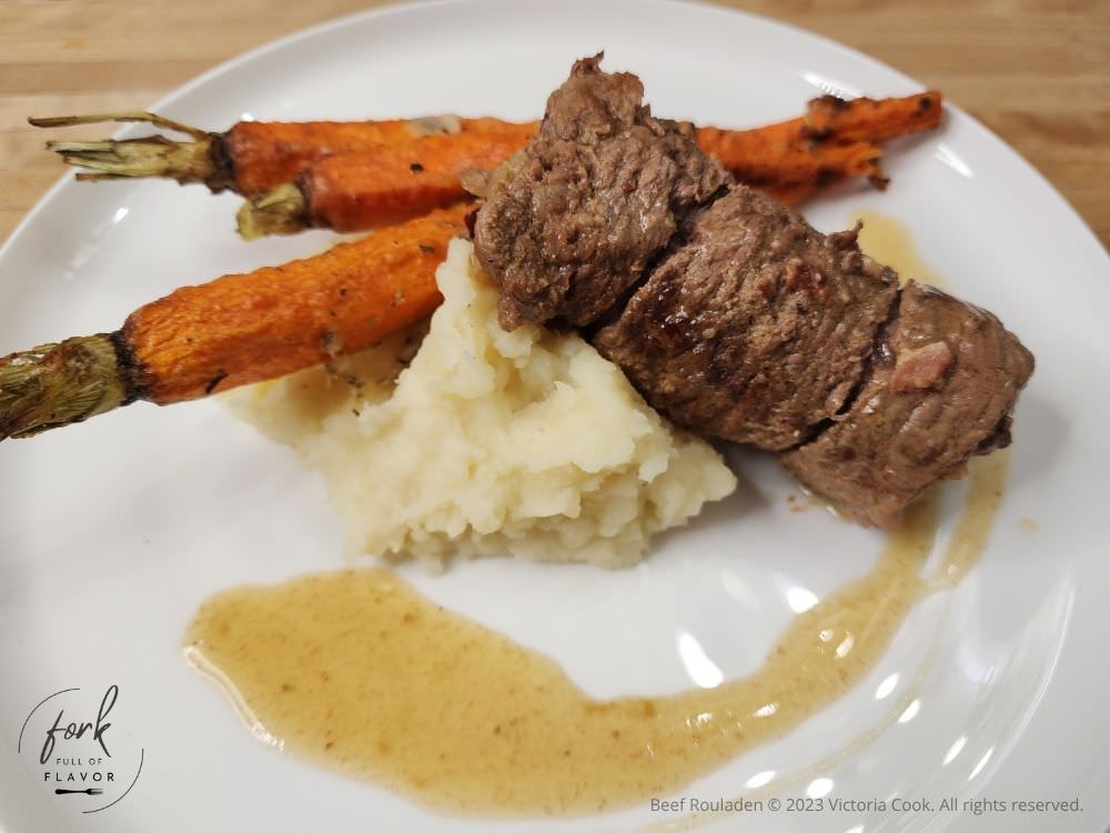 Beef Rouladen atop mashed potatoes and accompanied by roasted carrots on a plate.