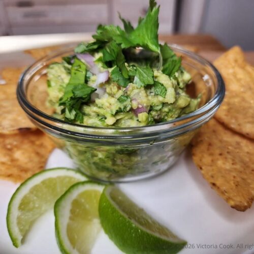 A bowl of fresh homemade guacamole surrounded by chips and a couple of limes.