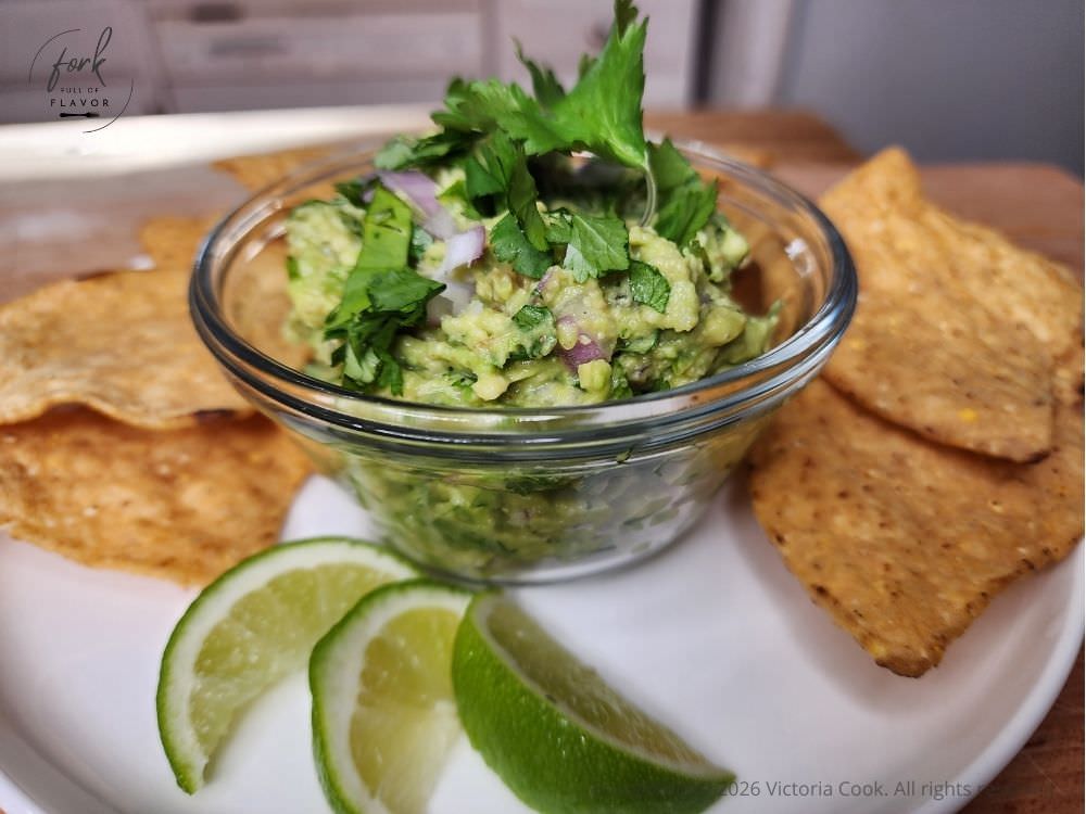 A bowl of fresh homemade guacamole surrounded by chips and a couple of limes.
